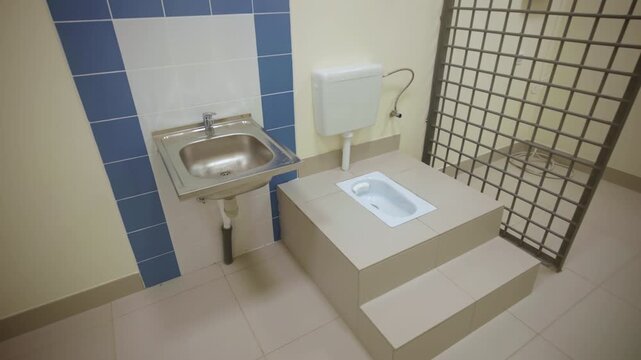 Public bathroom features tiled platform toilet steel basin and iron bars. Sanitary atmosphere highlights strict clinic conditions