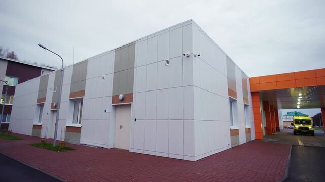 Modern building exterior shows white panel facade with orange entrance awning. Gloomy cloudy sky creates calm suburban atmosphere