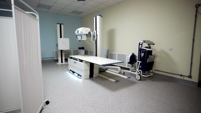 X-ray room corner shows digital radiography system with examination table. White privacy partition panels stand on clean clinical linoleum