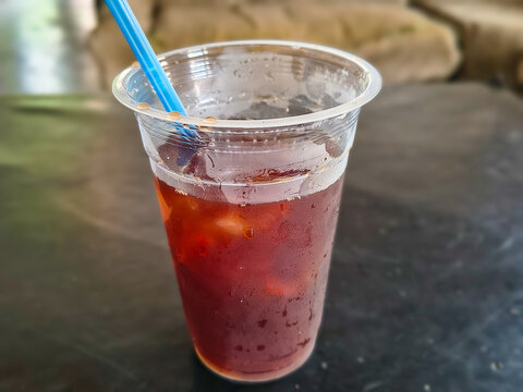 Fresh cold iced tea in a clear plastic cup with blue straw.