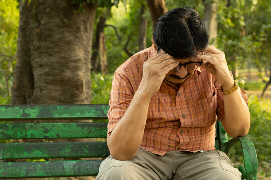 Thoughtful Indian mid aged man sitting alone on a park bench with a serious and worried expression. Concept of stress, anxiety, loneliness, mental health, retirement challenges, financial concerns.