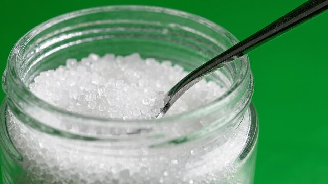 Close up of a glass jar filled with coarse white salt and a metal spoon