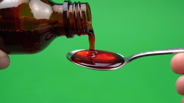 Pouring red cough syrup from a brown glass bottle into a metal spoon