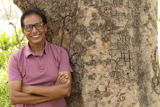 Happy Indian senior citizen smiling confidently with crossed arms in a lush green park. Portrait of a cheerful elderly man wearing eyeglasses, enjoying an active and healthy retirement lifestyle in a 