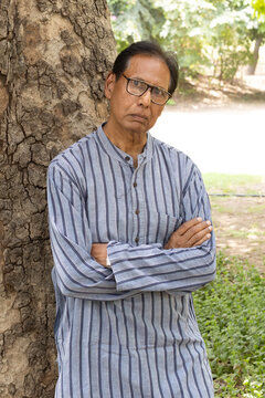 Sad Indian senior citizen sitting alone in a public park, looking thoughtful and emotional. Mature man wearing eyeglasses and traditional casual clothing, expressing loneliness, depression, aging.