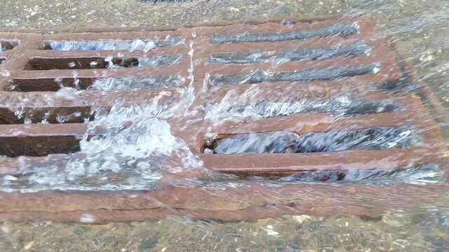 Water flowing into metal storm drain grate during rain. Urban infrastructure surface water drainage system for street flood prevention and heavy rainfall runoff management concept.