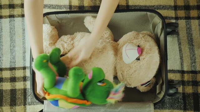 Child packs favorite stuffed toys into a suitcase for travel adventure.