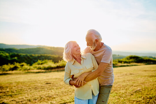 Loving senior couple smiling and embracing in a natural outdoor setting during sunset, symbolizing a happy, lasting relationship