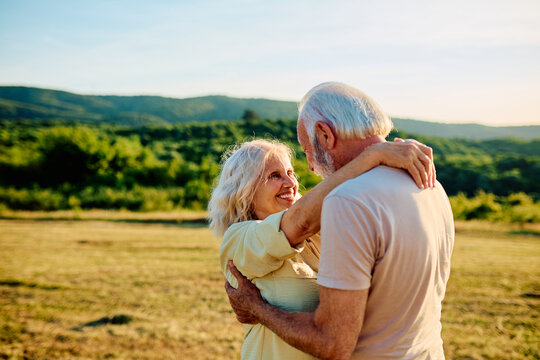 Senior couple embracing and dancing together in a field at sunset, sharing a loving moment in nature, full of happiness