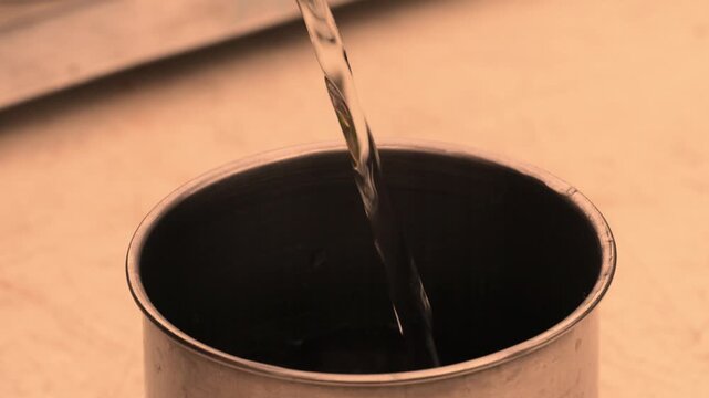 Close up water stream flowing into dark metal cup showing drinking water concept, hydration needs and access to clean resources with focus on essential liquid supply and everyday survival