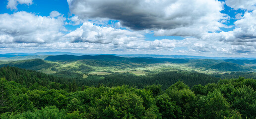 A panoramic view of green forests and hills under a cloudy sky. Bieszczady Mountains. View from the observation tower on Jeleniowaty. © Tomasz