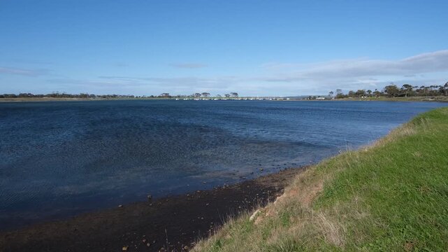 Waters of Hovells Creek, Corio, Australia with a green grassy bank curving along the shoreline. A tranquil, expansive sense of the Geelong-region waterway