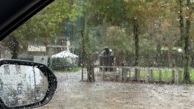 Rijeka, Croatia. Rainy view from car window showing blurred statue, green trees, and flooded ground in urban park setting