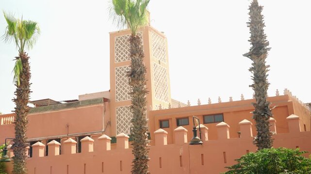 Sunlit Moroccan Minaret and Palm Trees Overlooking a Pink Medina Wall in Marrakech