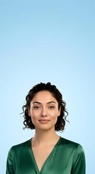 Young woman with shoulder-length curly dark hair and olive complexion wearing forest green v-neck top against clear blue background for professional headshot or corporate use.