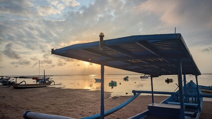 Traditional blue fishing boats anchored on a calm tropical beach at sunrise with golden sunlight reflecting on the water. © Ipramana