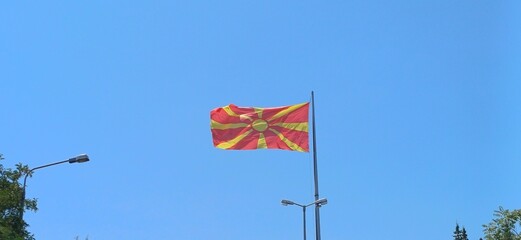 Fototapeta premium Flagge Nordmazedoniens im Wind vor klarem blauen Himmel mit Laternenmasten