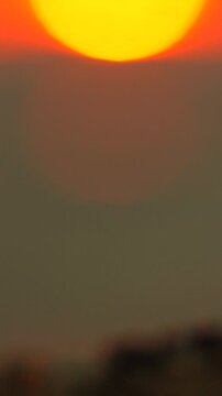 Golden sun globe descends toward the ocean horizon creating warm glowing reflections across rippling water. Vertical macro bokeh shot.