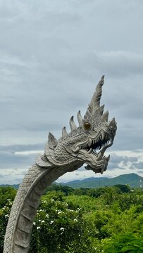 Carved stone dragon serpent statue head reaching toward a soft blue sky at a Thai temple