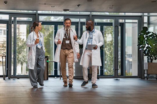 Three medical professionals walk in a hospital corridor while discussing patient care during a busy workday