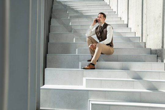 Business man talking on phone while sitting on stairs in a modern building