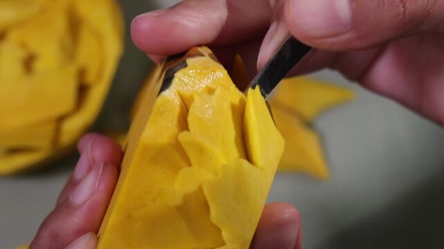 Close up human hand carving yellow fruit into intricate flower shape using small carving knife in Bangkok Thailand.