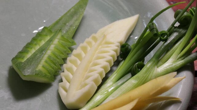 Close up human hand carving yellow fruit into intricate flower shape using small carving knife in Bangkok Thailand.