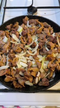Chopped chicken gizzards fry together with fresh sliced onions in a black pan on the stove top.