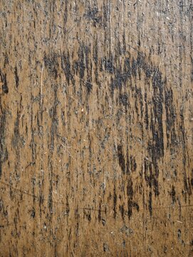 Weathered wooden surface with dark grain lines, scratches, rugged texture, and muted natural tones