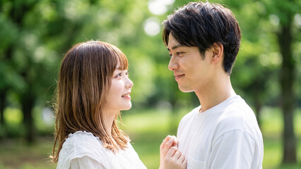 Fototapeta premium Young Japanese couple in love looking at each other romantically outdoors in a lush green park