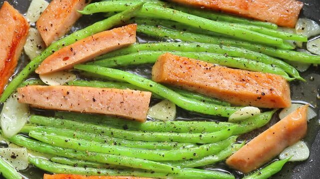 Stir-frying sliced bologna sausage with green beans and garlic in a hot pan. Top view shot
