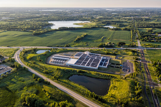 Aerial view of data center facility with solar panels on the roof, surrounded by green fields, ponds, and a winding road 
