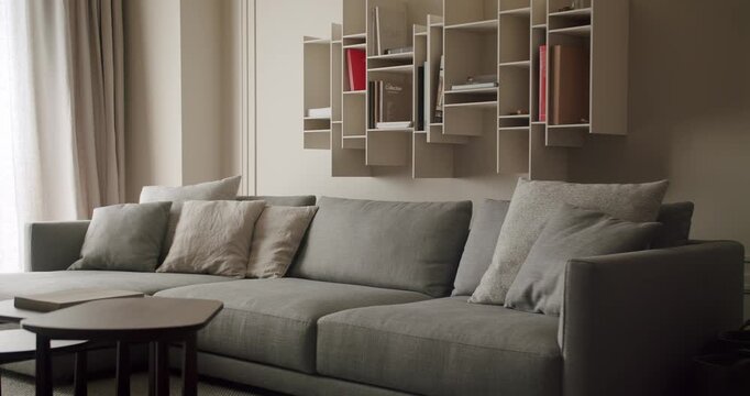 A contemporary living room features a comfortable grey sofa and unique wall-mounted bookshelves. Soft pillows add extra comfort to the minimalist space. Modern Living Room With Stylish Grey Sofa