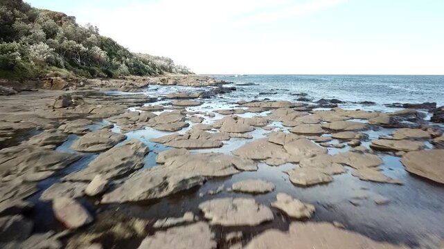 Drone flying low on a rocky beach in New South Wales Australia in Broulee Island