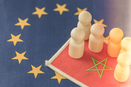 Morocco flag patch and wooden figures on the European Union flag background. Economic migration crisis, African refugees, international relations and EU external border.