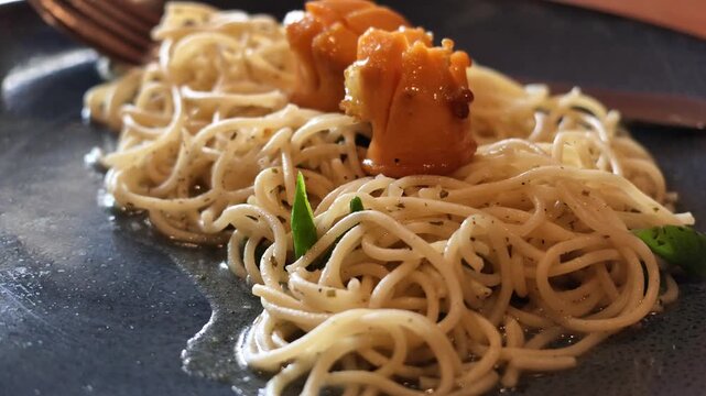 Slow motion low angle shot highlighting glossy spaghetti noodles coated in olive oil with sausage and herbs on a plate.
