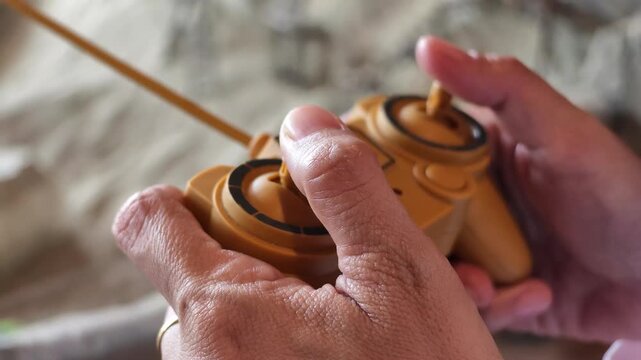 Slow motion close-up of adult hands holding and pushing joysticks on a yellow radio-controlled toy transmitter.
