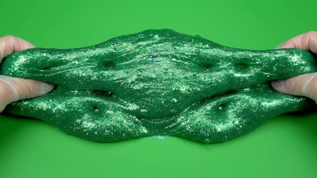 Hands in translucent gloves mold sparkly green slime on green background