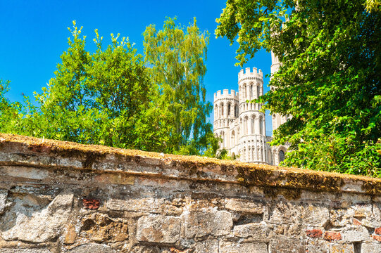 Unusual view of the famous Ely Cathedral towers seen framed between lush trees in the famous English city. Seen on bright summers day during drought.