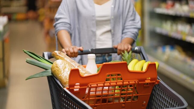 Woman pushing shopping cart filled with groceries in supermarket aisle