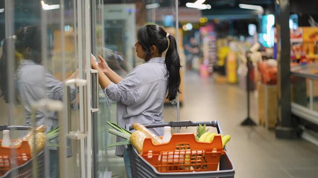 Woman choosing eggs from refrigerator in supermarket