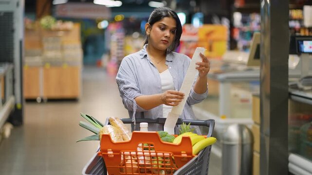 Indian woman checking shopping receipt in supermarket aisle