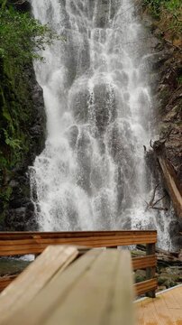 Vertical shot of a powerful waterfall viewed from a wooden viewpoint.
