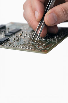 Technician using tweezers to place a surface mount component on a circuit board