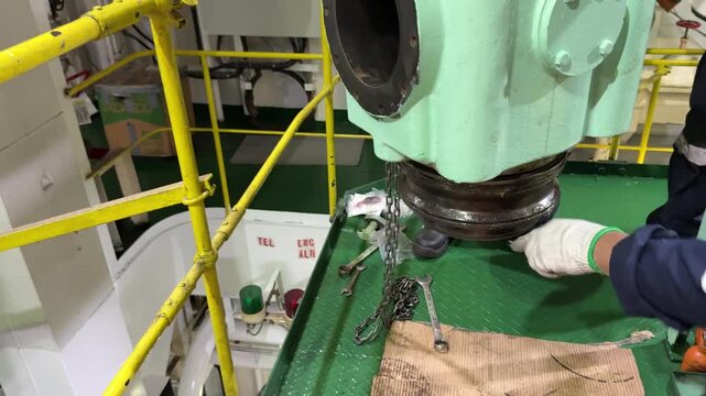 Large vessel main diesel engine cylinder cover suspended on crane hoist for scheduled maintenance and overhaul in engine room for maritime commercial fleet service concept