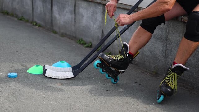 A middle-aged man's legs as he ties the laces of his roller skates to practice his hockey technique on the asphalt. Slow motion 4k footage.
