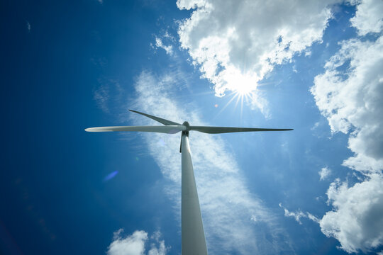 Wind Turbine Against Blue Sky with Sun Bursting Through Clouds