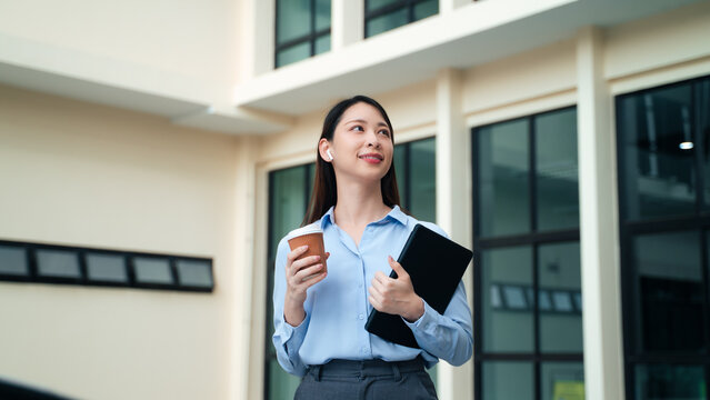 portrait of confident Asian businesswoman holding coffee cup and tablet standing outside office