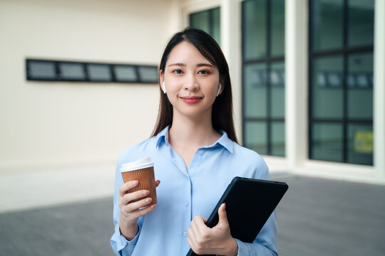 smiling Asian businesswoman looking at camera holding tablet and coffee cup