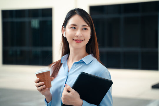 attractive Asian businesswoman smiling and looking side during coffee break outside office